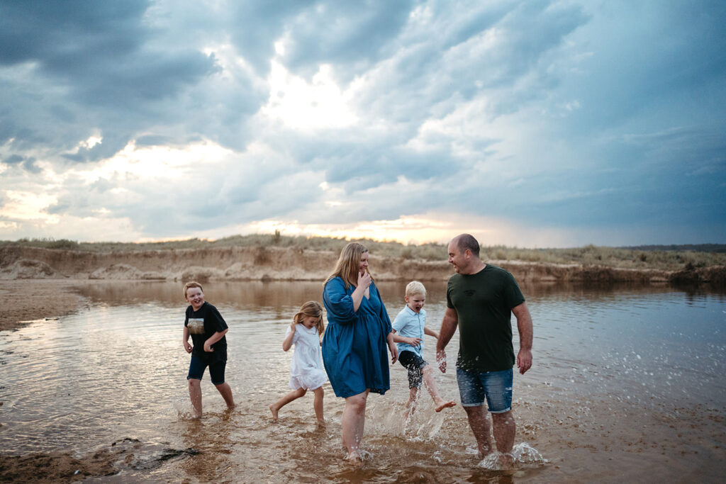 A family of five kick water at a shallow beach in sand in melbourne gippsland beaches
