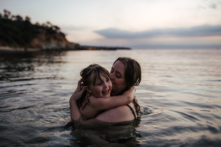 a mother holds her daughter in the ocean as the sun goes down at a family photoshoot in Melbourne