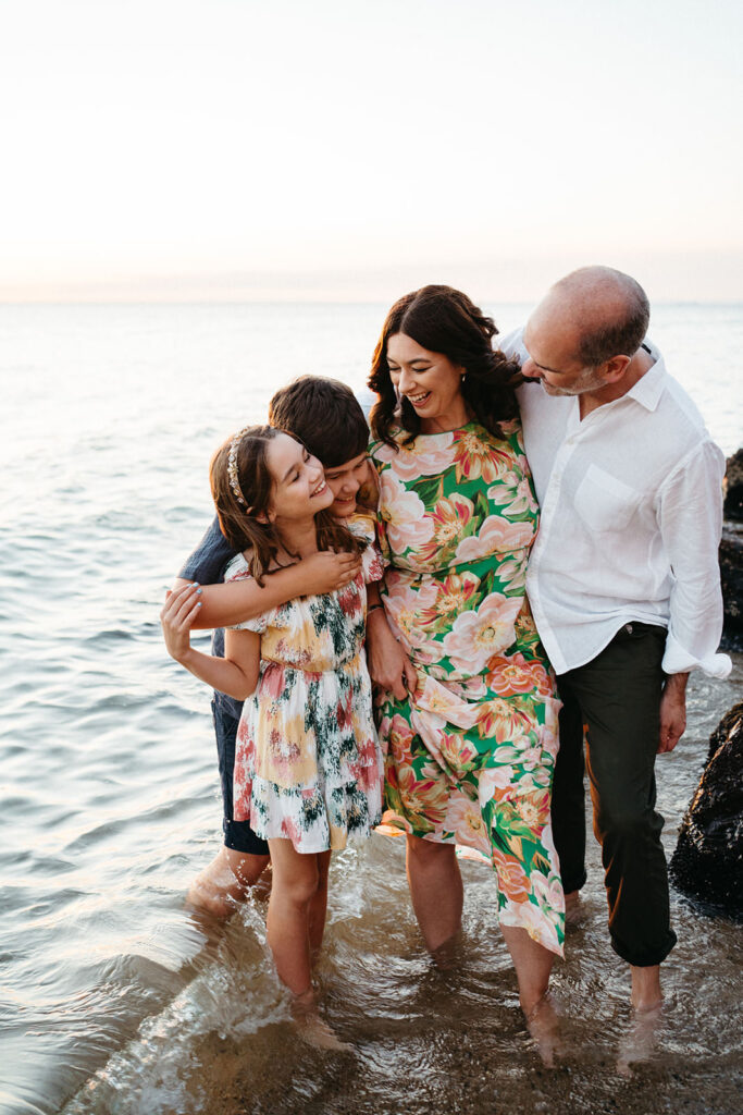 family at bayside beach black rock melbourne hugging and standing in the water they are smiling at eachother
