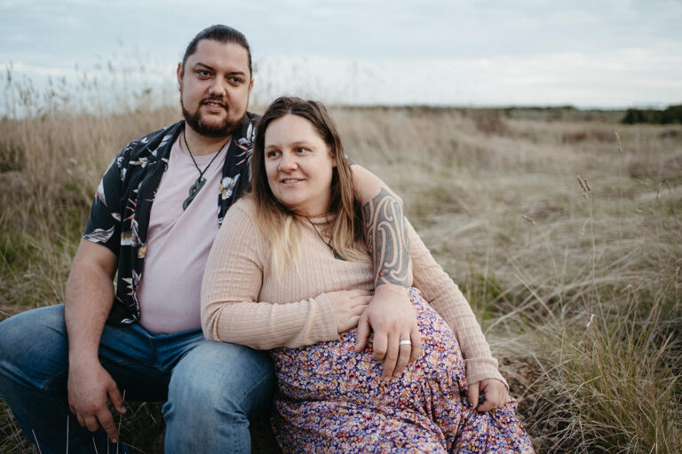 a couple sit in beachside she is pregnant and she he has his arm naturally around her