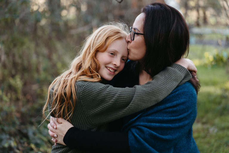 a mother kisses her teenage sons forehead, he has long hair