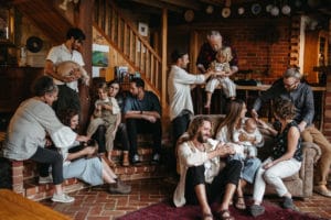 A large group of a melbourne family sit around inside a home interacting casually with each other