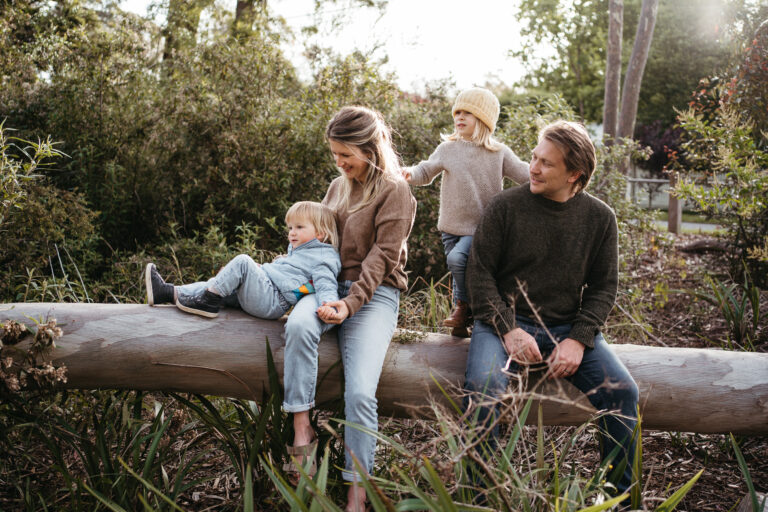 a family of four wearing cosy winter clothing sitting on a log