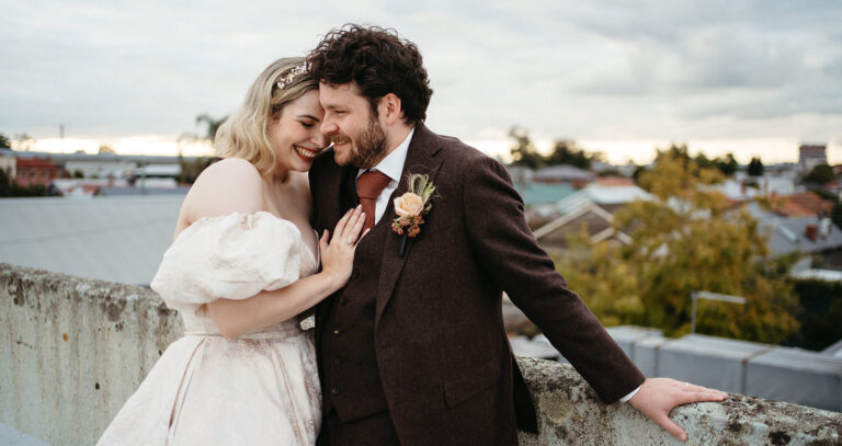 a bride leans into her groom on a rooftop in Melbourne she is wearing a vintage style dress with big puff sleeves