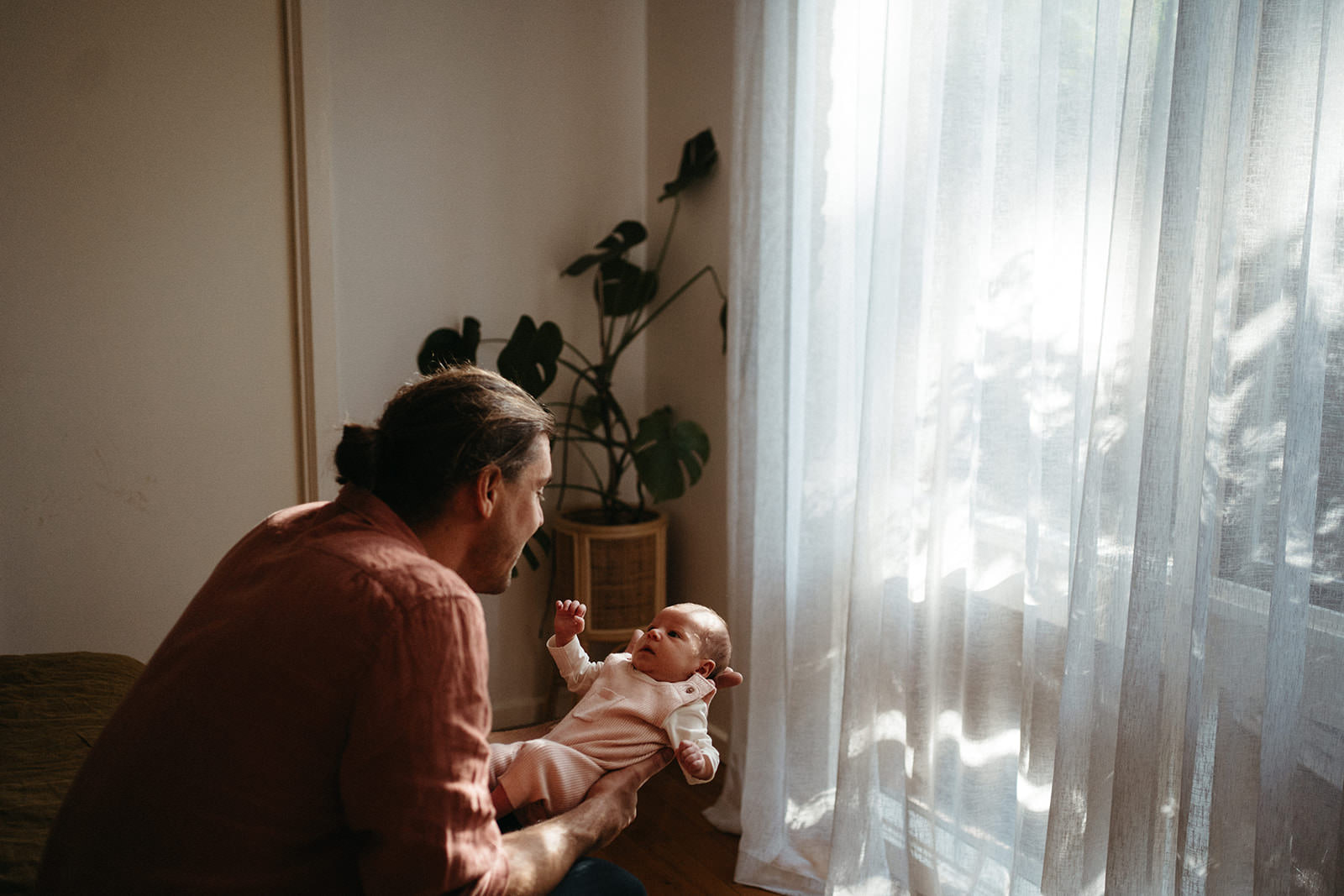 Father holding newborn daughter by window during natural, in-home newborn photography session in Melbourne