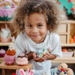 a curly haired boy holds some felt toys and smiles as he leans toward the camera