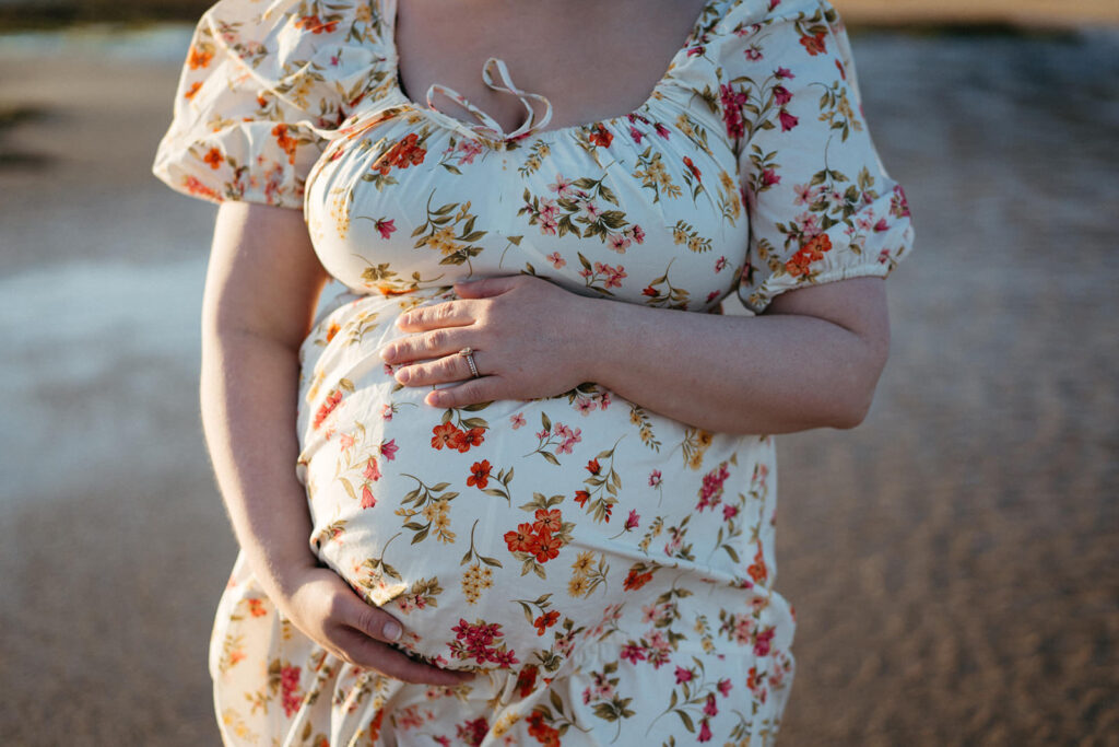 a close up of a woman in a floral dress with her hands on her pregnant belly