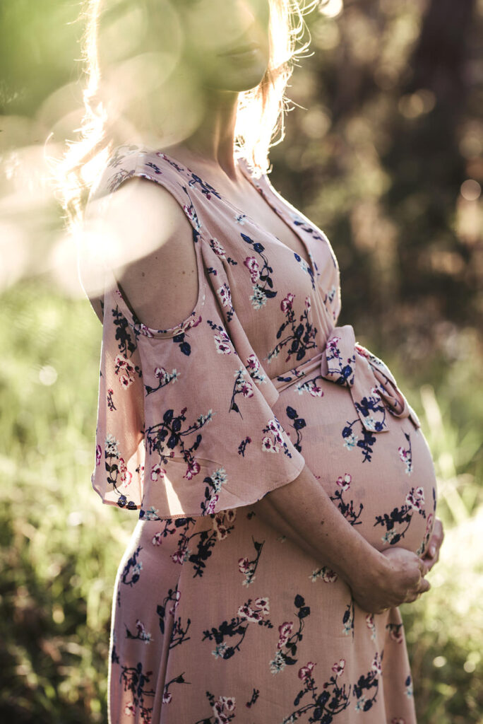 Maternity bump photo of a woman close up with light and leaves infront of her