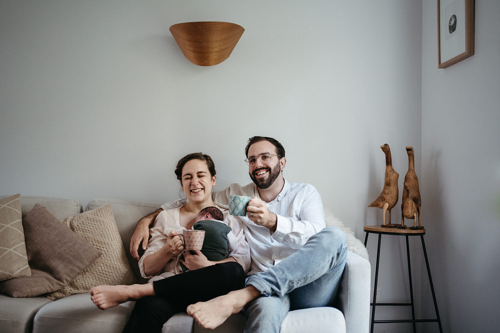 Couple laughing on couch with newborn during relaxed, natural newborn photography session in Melbourne home